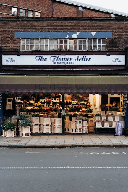 The storefront of The Flower Seller of Muswell Hill displaying a variety of fresh flowers arranged on wooden tables and shelves. The bouquets feature vibrant colors including yellow, orange, pink, and