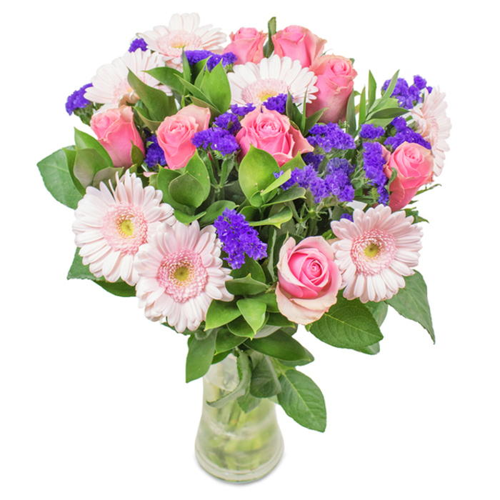A striking and elegant flower arrangement, this bouquet from a Kilburn florist artfully blends approximately 7 to 9 soft and medium pink roses-many displaying the delicate swirl of just-unfurled petals-with 5 to 7 pale pink gerbera daisies whose broad, ruffled blooms are luminous in natural light. Each flower is hand-selected, ensuring the roses and gerberas harmonise effortlessly, their pink tones elucidated by clusters of vivid purple statice or limonium. These purple fillers, scattered generously throughout, bring vibrant contrast and intriguing texture, making the bouquet pop while retaining sophisticated balance. Deep green foliage, glossy and full, forms a verdant foundation, evoking a sense of freshness reminiscent of walking past the flower stalls at Kilburn Market. The transparent vase showcases healthy, freshly cut stems floating in clear water, completing the arrangement's natural and inviting look. Perfect for special Kilburn occasions-birthdays, anniversaries, or even to brighten an office near the Jubilee Line-this arrangement conveys joy and affection. Every element speaks of dedicated craftsmanship, its local roots grounding it in the unique character and warmth of NW6.